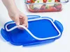 A hand is shown holding the lid of a blue food container, with a glass baking dish containing food in the background. Anteprima dell’immagine prodotto