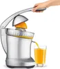 A hand is pressing down on a lever of a silver electric citrus juicer, with an orange half being juiced and orange juice pouring into a glass. Náhled obrázku produktu