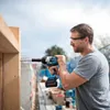 A man is using a cordless impact wrench to screw into a wooden beam outdoors. Podgląd zdjęcia produktu