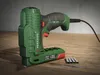 A green electric tacker is placed on a wooden surface. Produktbild-Vorschau