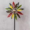 A colorful metal wind spinner shaped like a flower, mounted on a black stake, against a textured gray background. Produktbild-Vorschau