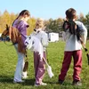 Three children are walking in a grassy field, each carrying a hobby horse. Náhľad obrázku produktu