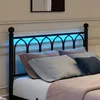 A close-up view of a black metal bed frame with blue LED lighting in the headboard, adorned with pillows and a pink blanket. Produktbild-Vorschau