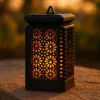 A solar lantern with a flame effect sits on a stone surface outdoors at dusk. Podgląd zdjęcia produktu