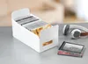 A white CD storage organizer filled with CDs, and a pair of headphones and a stack of CDs are on a gray surface next to it. Produktbild-Vorschau