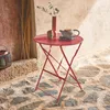 A red bistro table with a teapot and vase on it, set on a stone patio. Anteprima dell’immagine prodotto