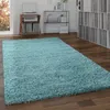 A shaggy blue rug is placed on a wooden floor in a room with shelves of records and a turntable. Produktbild-Vorschau