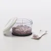 A clear studio shot of a manual food chopper filled with chopped red onions, with its lid resting beside it and a small spoon with chopped onions to the right. Produktbild-Vorschau