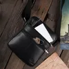 A black leather messenger bag is shown on a wooden surface, with a notebook, pen, and keys inside. A vintage-style map and a painting of a canal city are also visible. Podgląd zdjęcia produktu