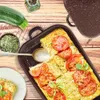 A prepared zucchini casserole with tomatoes and herbs, served with a spoon and a side dish, on a wooden table with ingredients. Produktbild-Vorschau