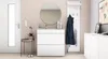 A hallway with a white shoe cabinet, a round mirror, a coat rack with a coat, and a small side table with a plant. Produktbild-Vorschau