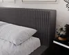 A close-up view of a dark gray upholstered headboard with a white pillow on a bed. Náhľad obrázku produktu