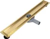 A linear shower drain with a gold-colored grate and a gray plastic drain body, shown from a diagonal angle against a white background. Náhled obrázku produktu