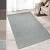 A light gray carpet is laid out on a light wooden floor in a room with white curtains and a sofa in the background. Produktbild-Vorschau