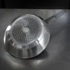 The underside of a frying pan is shown resting on a metallic surface. Podgląd zdjęcia produktu