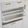 A close-up view of a white shoe cabinet with gold handles, showing two drawers and two flip-down shoe compartments. Produktbild-Vorschau
