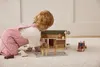 A young child plays with a wooden farm toy set on a carpeted floor. Produktbild-Vorschau
