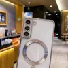 A close-up shot of the back of a white smartphone case with a silver magnetic ring and camera protection, set against a blurred background of a cafe or restaurant. Anteprima dell’immagine prodotto