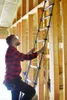 A man is climbing an extendable ladder inside a house under construction. Produktbild-Vorschau