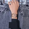 A person's wrist wearing a rose gold watch is shown against a background of denim jeans. Produktbild-Vorschau