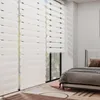 A bedroom scene with a bed and large white blinds. Voir les images du produit