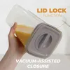 A hand holds a clear container filled with orange liquid, showcasing its lid and features. Produktbild-Vorschau
