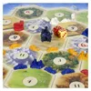 A close-up view of a board game, likely Settlers of Catan, with game pieces and dice on the board. Náhled obrázku produktu