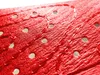A close-up view of a red, textured material with small holes and stitching. Produktbild-Vorschau