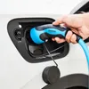 A hand is shown plugging a blue and black Mennekes electric vehicle charging cable into a white car. Produktbild-Vorschau