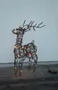 A wireframe reindeer decoration with LED lights sits on a wooden surface in front of a textured wall. Podgląd zdjęcia produktu
