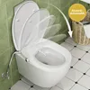 A modern bidet toilet seat is shown in a bathroom setting with green tiled walls and a black and white tiled floor. A wicker basket is visible in the background. Anteprima dell’immagine prodotto