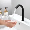 Hands washing under a black automatic faucet in a modern bathroom sink. Náhled obrázku produktu