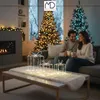 A couple sits on a couch in a living room decorated for Christmas, with Christmas trees and a fireplace visible. Decorative gift boxes with lights are on the coffee table. Podgląd zdjęcia produktu