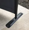 Close-up of the base of a dark gray fabric screen, showing its metal support pole and a flat metal base plate attached to the ground. Produktbild-Vorschau