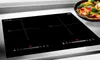 A black induction cooktop with red digital displays and cooking zone indicators, placed on a light gray countertop. A bowl of colorful stir-fried vegetables is visible in the background. Voir les images du produit