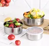 Three stainless steel food containers filled with various food items, including tomatoes, lettuce, olives, corn, and carrots, are arranged on a white surface with a wooden board and some paper. Produktbild-Vorschau