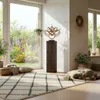 A bright and airy room with a large window overlooking a garden, decorated in a bohemian style with plants, cushions, and a decorative sculpture on a wooden pedestal. Produktbild-Vorschau