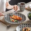 A person is eating a meal with shrimp and vegetables from a patterned plate, with a mug and other dishes visible. Náhled obrázku produktu
