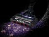 A close-up of a vacuum cleaner head with lights illuminating dirt on a grid-like surface. Produktbild-Vorschau