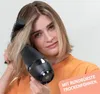 A woman is drying her hair with a hairdryer and a round brush. Produktbild-Vorschau