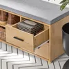A close-up view of a wooden shoe bench with a gray upholstered top, showing an open drawer with a tissue box inside. Produktbild-Vorschau