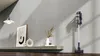 A modern living room with a vacuum cleaner standing against a wall, next to a shelf with decorative items. Náhled obrázku produktu
