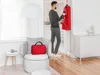 A man is steaming a red coat in a modern living room. Produktbild-Vorschau