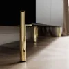 Close-up of the legs and bottom edge of a black TV cabinet with gold legs, resting on a wooden floor. Produktbild-Vorschau