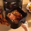 A hand is shown removing a basket of food from an air fryer. Produktbild-Vorschau