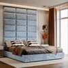 A well-lit bedroom with a large, upholstered headboard and a bed dressed with pillows and a blanket. Anteprima dell’immagine prodotto