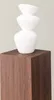 A white abstract sculpture stacked on a brown wooden pedestal. Produktbild-Vorschau