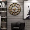 A large gold Roman numeral wall clock hangs on a gray brick wall above a black leather armchair. Produktbild-Vorschau