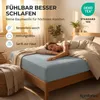 A woman sleeping on a bed with a grey fitted sheet. Produktbild-Vorschau