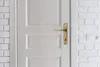 A white door with a gold handle is shown next to a white brick wall with an electrical outlet. Anteprima dell’immagine prodotto